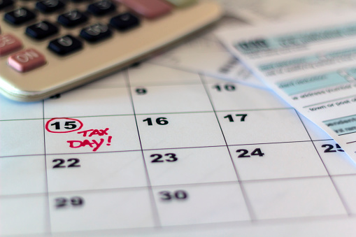 Tax day marked on calendar, calculator and tax form on desk