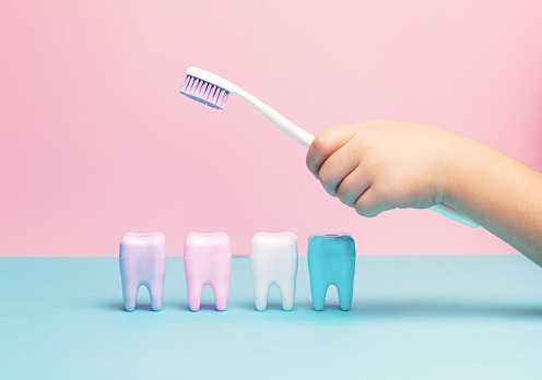 Child's hands holding big tooth and toothbrush on pink backgroubd. Healty care teeth concept. Top view, flat lay. Copy space for your text.