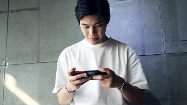 Young asian man standing playing a game on the phone with happiness
