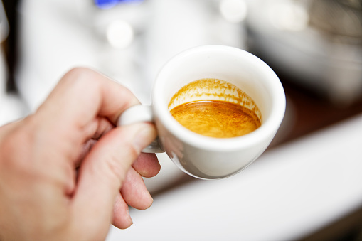 Humans hands holding white cup of coffee espresso against blurred background. Shallow focus.