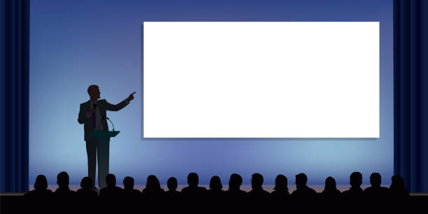A standing leader on stage, presents his project to an audience During a conference, a businessman standing behind a desk, points his finger at a white screen to present a project in front of an audience. business plan document stock illustrations