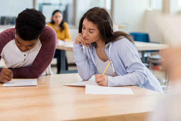 High school student cheats on test Dishonest female high school student copies an answer from a classmate's paper during an exam. high school high school student science multi ethnic group stock pictures, royalty-free photos & images