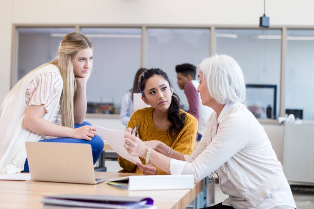 High school teacher has serious conversation with students Serious female high school science teacher shows something on a homework to two female students. high school high school student science multi ethnic group stock pictures, royalty-free photos & images