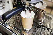 Closeup of espresso pouring from coffee machine in cardboard cup