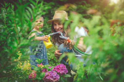 Happy child and his mother watering plants  in spring or summer day