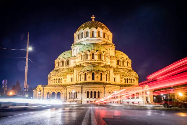 Wide angle photograph of Alexander Nevsky Cathedral, downtown district in city of Sofia, capital of Bulgaria, Eastern Europe. Long exposure during night time with the evening illumination of the building and light trails from the passing traffic. Shot on Canon EOS R full frame system RF premium lens.