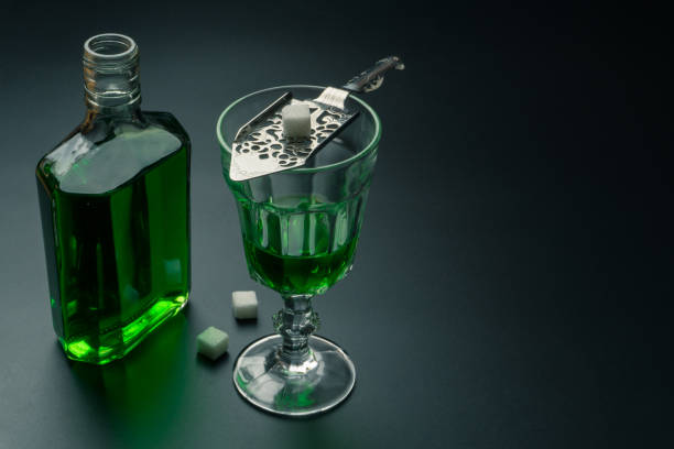a glass of absinthe and a stainless steel slotted spoon a glass of absinthe and a stainless steel slotted spoon with the sugar cubes, the absinthe bottle on the table, selective focus absinthe spoon stock pictures, royalty-free photos & images