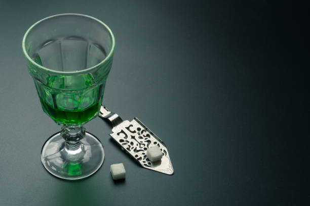 a glass of absinthe and a stainless steel slotted spoon a glass of absinthe and a stainless steel slotted spoon with the sugar cubes on the table absinthe spoon stock pictures, royalty-free photos & images