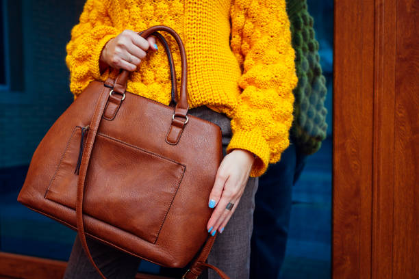 Young woman holding stylish handbag and wearing yellow sweater. Spring female clothes and accessories. Fashion Young woman holding stylish handbag and wearing yellow sweater while looking at watch. Spring female clothes and accessories. Fashion spring fashion stock pictures, royalty-free photos & images
