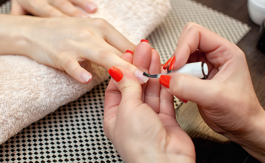 El artista de uñas pinta clavos con esmalte de uñas durante el procedimiento de extensiones de uñas con gel en el salón de belleza. Cuidado profesional de las manos. photo