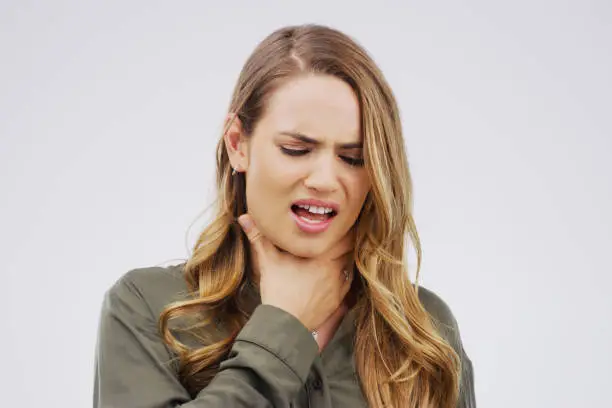 Studio shot of a young woman suffering with a sore throat against a grey background