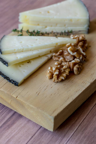 Tasty cheese on a table with nuts and fresh thyme branches. Rustic mediterranean appetizer table with manchego cheese.