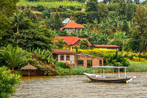 Barco de techo anclado en la costa con pueblo rwandés en el fondo, lago Kivu, Ruanda photo