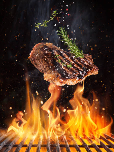 Tasty beef steaks flying above cast iron grate with fire flames. stock photo