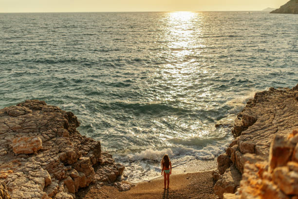 istock Girl standing alone on beach at sunset 1140181852