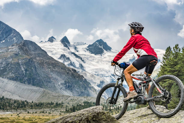 Mountainbiking in Engadine valley Switzerland active senior woman, riding her e-mountain bike in the Roseg valley below the glaciers and summits of the Sella Group and Piz Roseg graubunden canton photos stock pictures, royalty-free photos & images