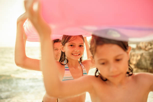 Mother enjoying day on the beach with her son and daughter while taking inflatable mattress out of water at sunset.