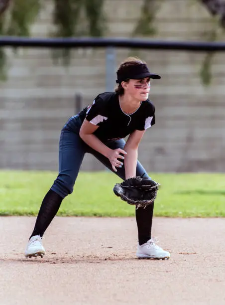 Alert female softball infielder crouched down into ready position and prepared for the ball.