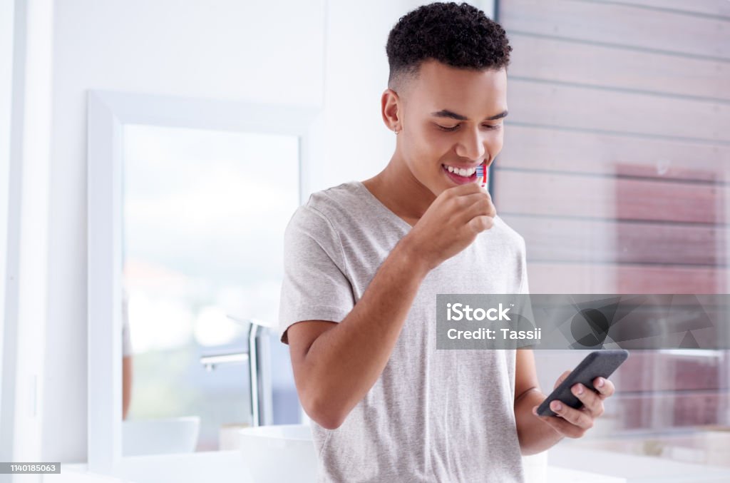Fresh day, fresh new social network updates Shot of a handsome young man brushing his teeth at home Brushing Teeth Stock Photo