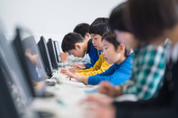 学校でコンピュータを使うことを学ぶ小学生のグループ - media studies ストックフォトと画像
