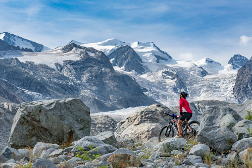 Senior woman, riding her e-mountain bike on the trail to the Morteratsch glacier near Pontresina , Engadin, Switzerland,Alps. In the background the famous mountains of Piz palu,