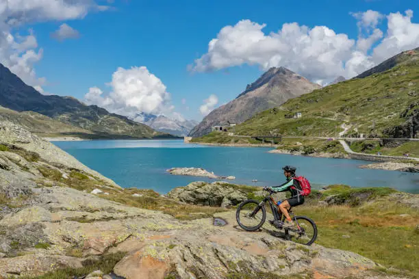 senior woman, riding her e-mountainbike on the famous Bernina express trail at Lago Bianco, Bernina Pass near Pontresina an St.Moritz, Engadin, Switzerland