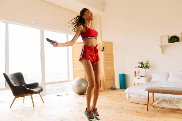 mujer vistiendo shorts rojos y la parte superior saltando la cuerda en casa - saltar actividad física fotos fotografías e imágenes de stock