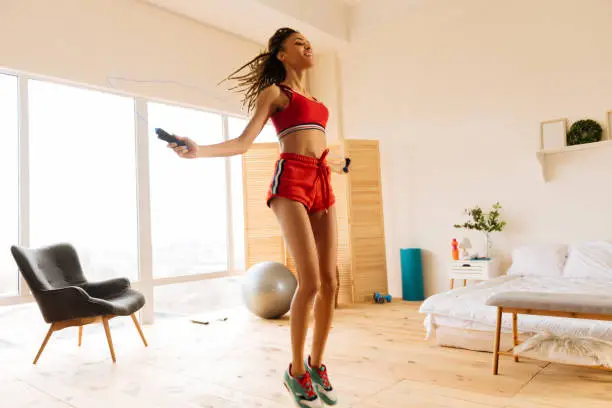 Photo of Woman wearing red shorts and top skipping the rope at home