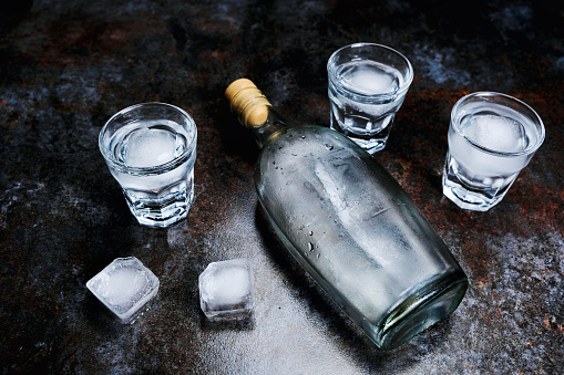 Bottle of vodka with shot glasses and ice. On stone background. Copyspace.