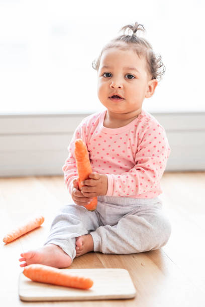 linda niña sentada en el suelo y jugando con una zanahoria - baby carrot fotografías e imágenes de stock