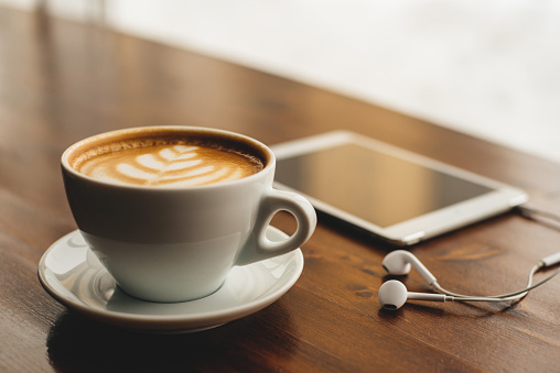 Tablet, headphones and cappuccino on brown wooden surface