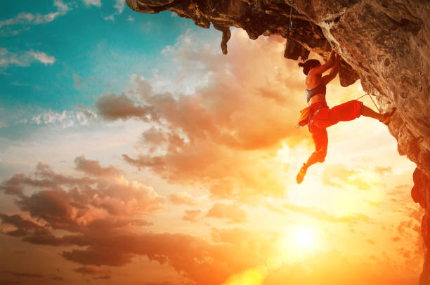 istock Athletic Woman climbing on overhanging cliff rock with sunset sky background 1140200162