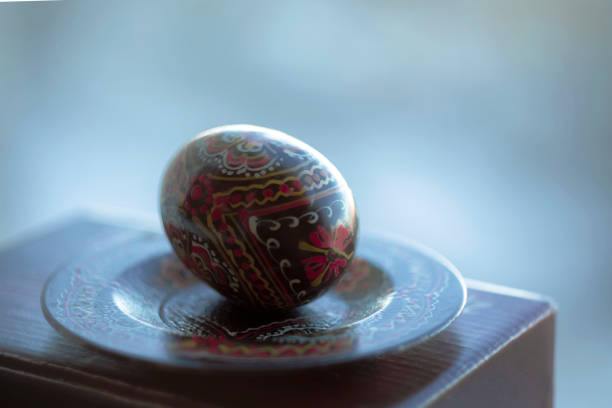Easter egg on a plate painted in black with a homemade pattern. Closeup view on blurred background with copy space for text, Easter wallpaper concept.
