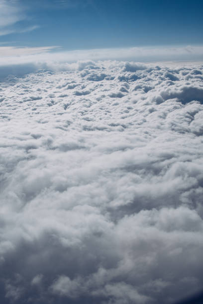 istock Airplane window view over horizon covered by white clouds beneath sunny blue sky. 1140203602
