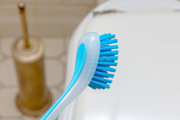 hand in a yellow rubber glove and brush for cleaning against the background of tiles in the toilet room.