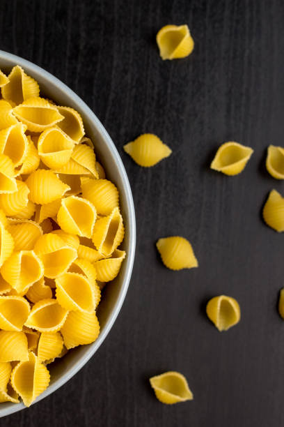 istock Top view of black background with italian raw conchiglie paste shells in bowl with copy space 1140213341