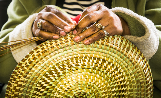 Charleston, South Carolina, USA -March 26, 2019-A craftsperson in the Charleston City Market creates a beautiful sweetgrass basket from locally grown grasses and bull rushes in much the same way people in the Charleston area have done for over 300 years.