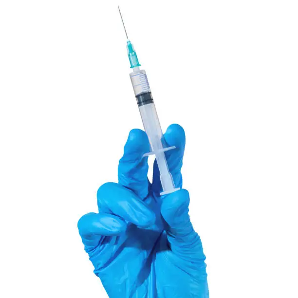 Photo of a hand in blue glove holding a syringe with clear liquid on a white background.