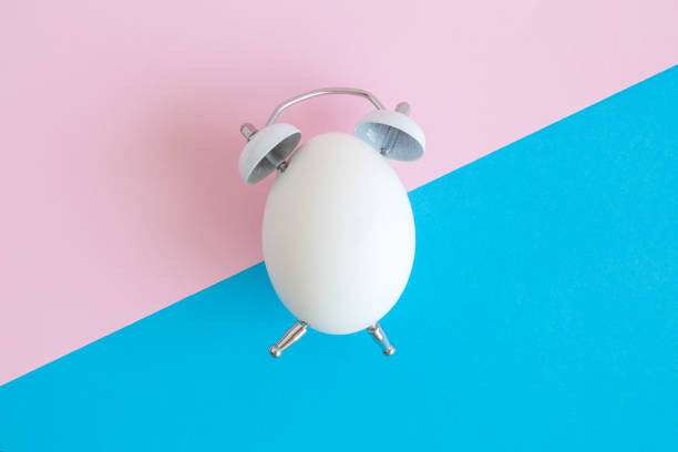 Flat lay of white egg in form of alarm clock on pastel background minimal easter time creative concept.