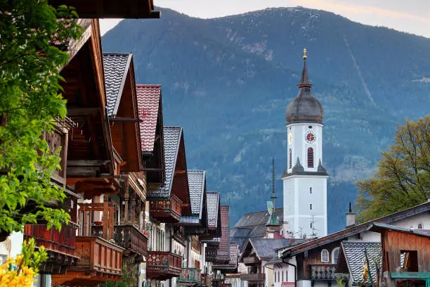 Row of typical German houses with wooden balconies in historic center of Garmisch-Partenkirchen with domed parish church St Martin and Wank mountain in Estergebirge, Bavarian Prealps Bayern Germany Europe