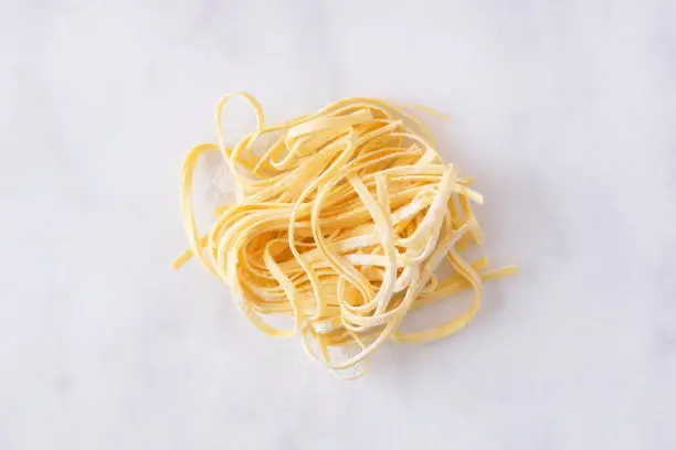 Nest of fresh linguine pasta, top view against a white marble background