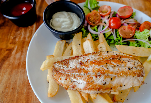 Close up shots of fresh fish and chips with fries, salad and tartar sauce on table