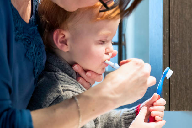 симпатичные рыжий мальчик малыша, имеющих зубы щеткой его мать - dental floss brushing teeth dental hygiene dental equipment стоковые фото и изображения