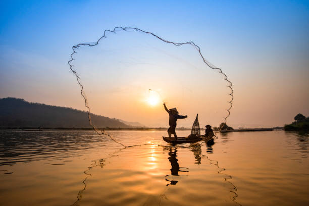 Asia fisherman net using on wooden boat casting net sunset or sunrise in the Mekong river Asia fisherman net using on wooden boat casting net sunset or sunrise in the Mekong river / Silhouette fisherman boat with mountain background people life on countryside laos photos stock pictures, royalty-free photos & images