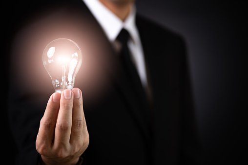 Business concept. Businessman holding lamp Light bulb against dark background.