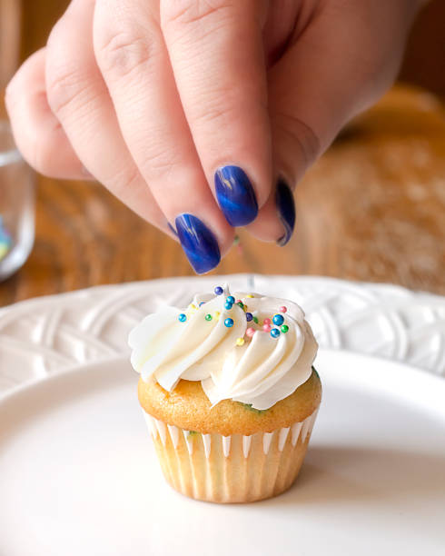 istock Dropping pastel colored sprinkles onto a freshly frosted mini cupcake.  Hand only. 1140272878