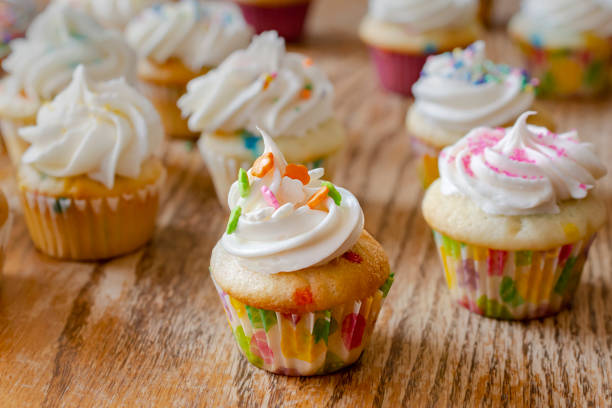 Various mini cupcakes decorated in spring and Easter colors.  Background of a rough wood table.