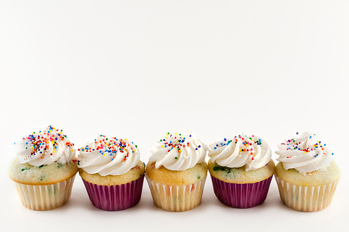 Five mini cupcakes in a row isolated on white background.  Confetti cake with white icing with rainbow sprinkles. Copy space above.