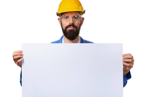 istock Handsome bearded man worker in protective helmet holding white advertising banner with copy space, isolated on white background. 1140277836
