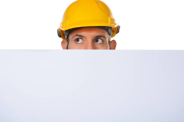 istock Half face of worker in protective construction yellow helmet with white advertising board, isolated on white background. 1140277837
